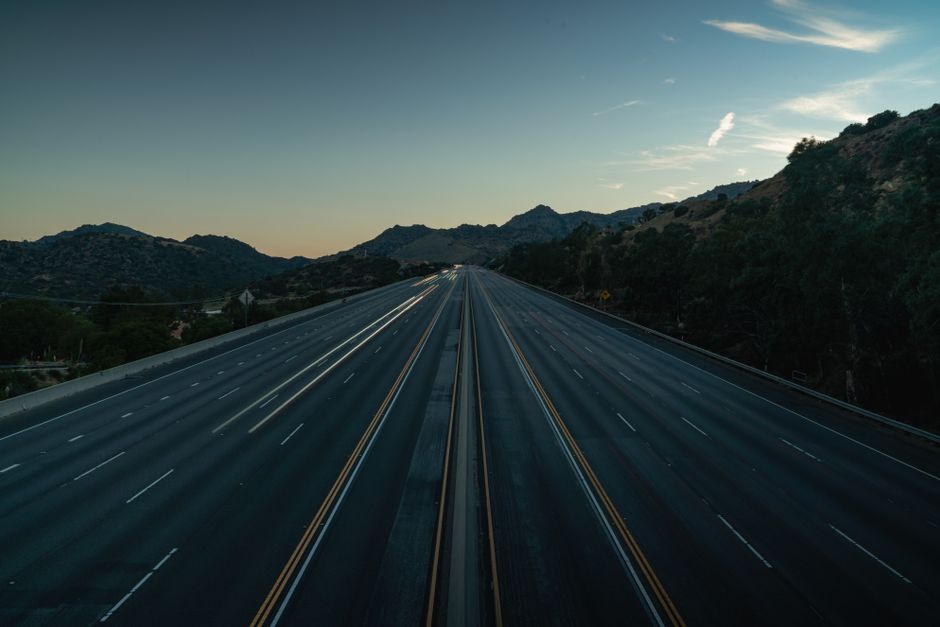 A serene aerial view of an empty mountainous highway at dusk, showing the vastness and tranquility.